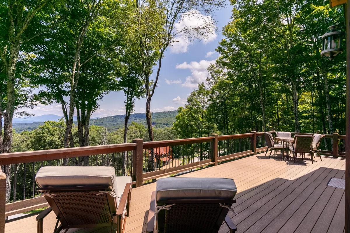 A spacious deck furnished with lounge chairs overlooks lush green trees and distant rolling hills. The setting is peaceful and inviting, offering a secluded spot to unwind while taking in nature’s beauty and mountain views.