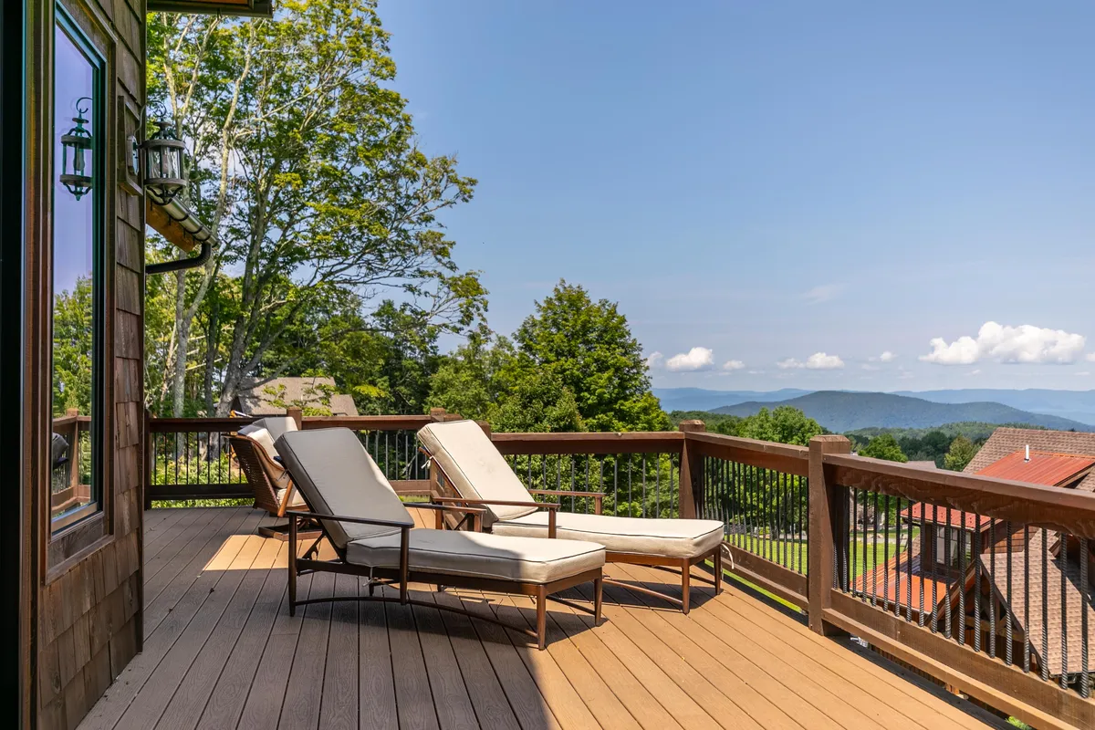 A spacious outdoor deck furnished with lounge chairs overlooks a sweeping vista of rolling mountains and lush greenery. The scene is serene, with the deck railing framing the panoramic views, ideal for watching sunsets, stargazing, or hosting lively gatherings against a breathtaking natural backdrop.