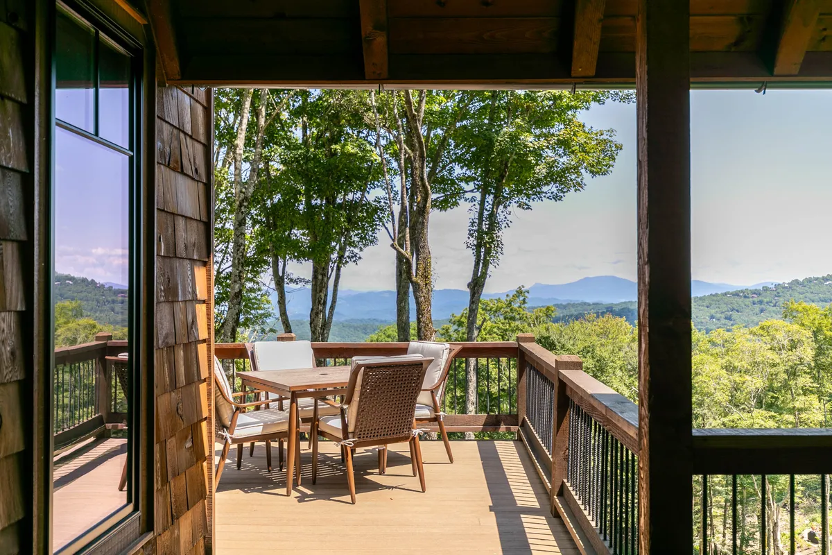 A spacious wooden deck overlooks sweeping mountain views and lush greenery, with an outdoor dining set inviting guests to relax, dine, or socialize in the fresh air. The setting is serene and inviting, ideal for gatherings after enjoying community activities.
