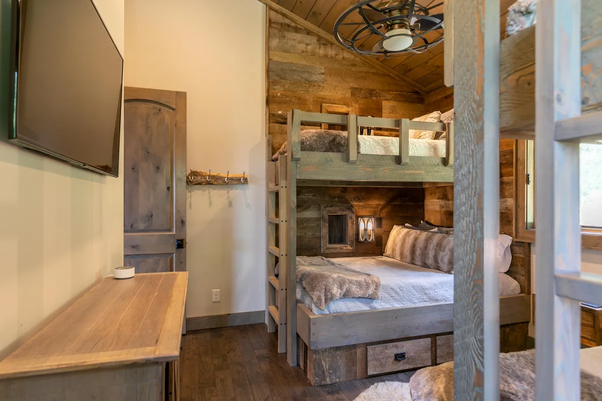 This interior image focuses on a cozy bunk room with wooden walls, multiple bunk beds, a large TV, and a wooden dresser. The relaxed mood is perfect for storytelling, games, and family bonding after a day outdoors.