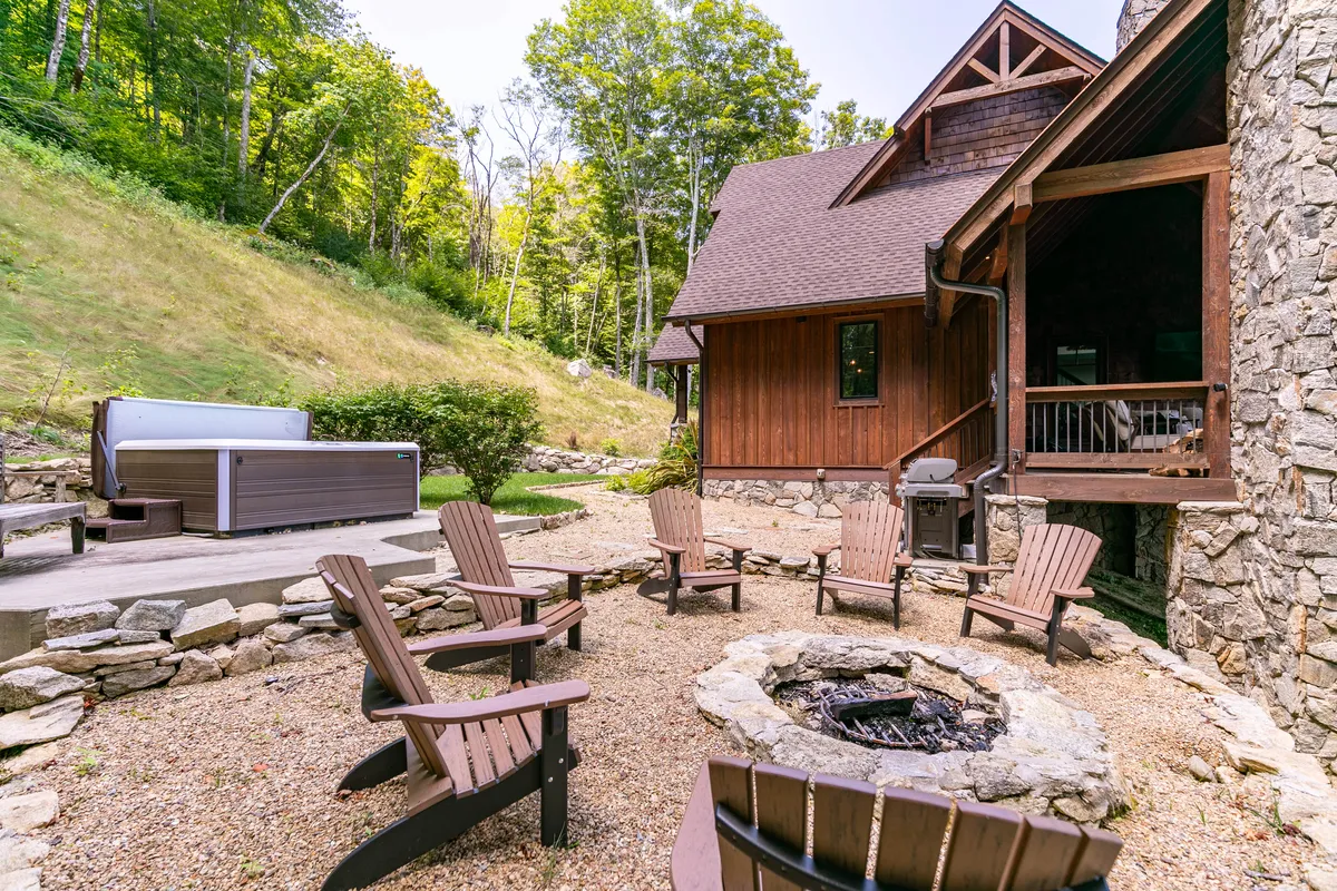Featuring a cozy fire pit area, outdoor seating, a hot tub, and the wooden house facade, this photo evokes evening gatherings, relaxation after a day full of activities, and the social connection central to the amenities experience.